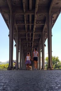 Low angle view of sisters holding hands and walking on road under bridge