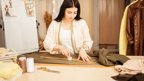 Black haired seamstress in atelier, portrait at work. table with fabric and sewing tools, 