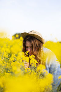 Full length of woman smelling yellow flowers against sky