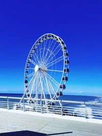 Ferris wheel by sea against clear blue sky