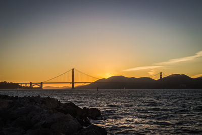 Silhouette bridge over sea against sky during sunset