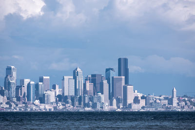 Sea by modern buildings in city against sky