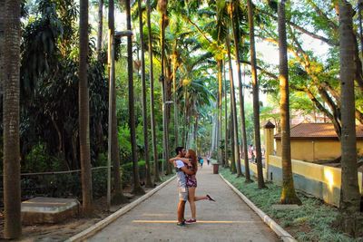 Full length of young couple kissing on footpath amidst palm trees