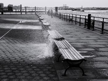 Empty bench on pier by sea against sky in city