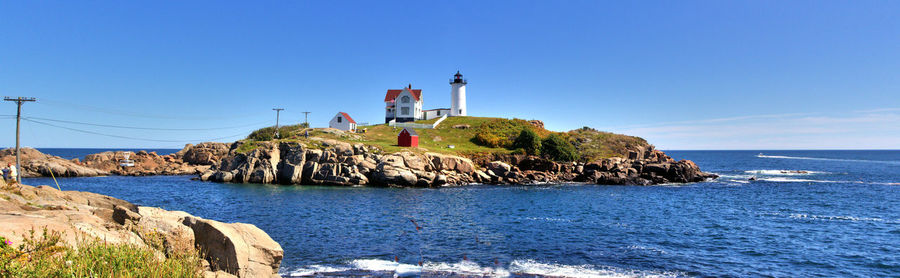 Lighthouse by sea against clear blue sky