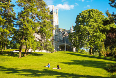 People sitting on park by building against sky