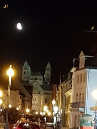 Illuminated street amidst buildings against sky at night