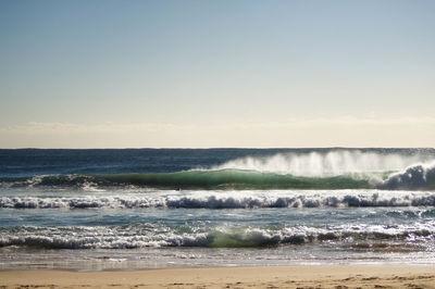 Waves rushing towards shore against sky