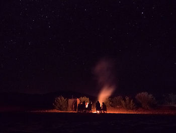Silhouette people on illuminated land against sky at night