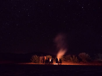 Silhouette people by campfire against sky at night