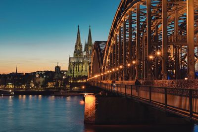 Illuminated bridge over river amidst buildings in city