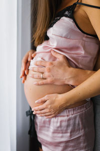 Expectant father hugs pregnant wife, close-up of arms and stomach