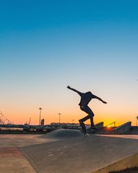 Rear view of man skateboarding on street against clear sky during sunset