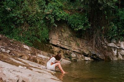 Woman sitting on tree by water