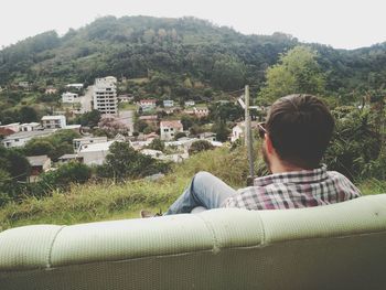 Rear view of man sitting on buildings against trees