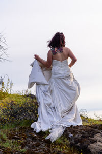 Rear view of young woman in wedding dress standing against sky