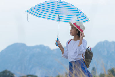 Full length of young woman holding umbrella standing on rainy day