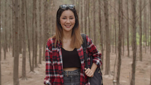 Portrait of smiling young woman standing against trees