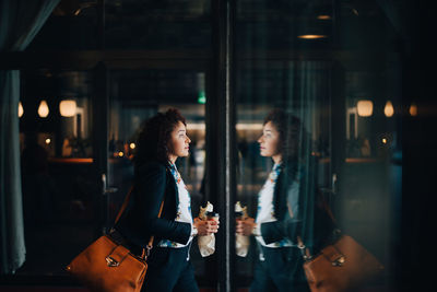 Side view of mid adult businesswoman holding food and drink while walking in cafe