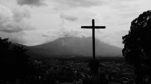 Cross amidst trees and buildings against sky