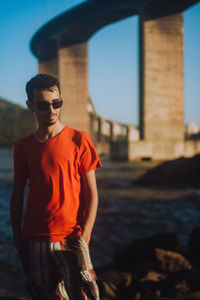 Young man wearing sunglasses standing against city in background