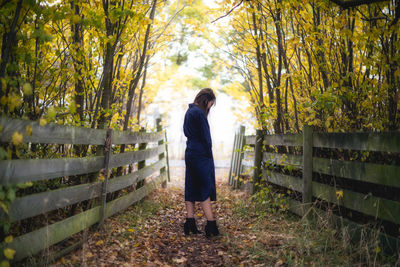 Woman looking down while standing amidst trees during autumn