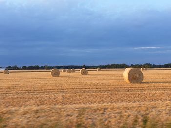 Hay bales on field against dramatic sky