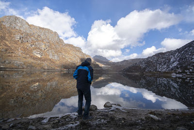 Rear view of mature man standing at lakeshore against cloudy sky