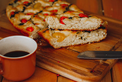 Homemade italian focaccia cut into slices, with tomato and olive oil and a cup of coffee.