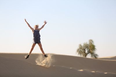 Portrait of girl jumping on sand dune at desert against clear sky