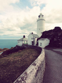 Lighthouse by sea against buildings against sky