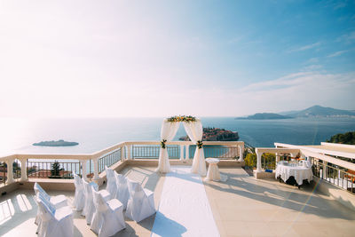 Chairs and tables at swimming pool against sky