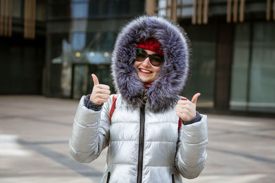 Happy young woman in winter jacket with backpack near building