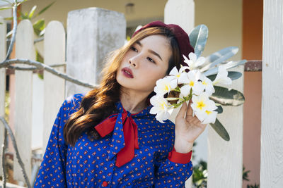 Young woman holding flower looking away while standing outdoors