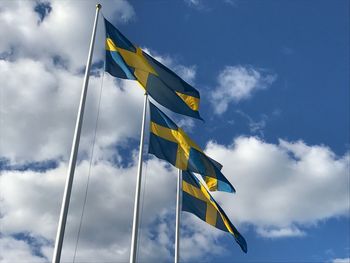 Low angle view of flags waving against cloudy sky