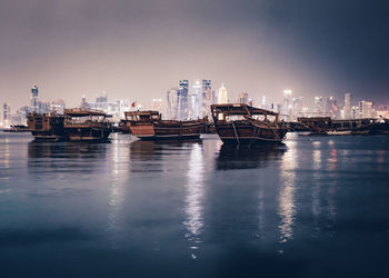 Illuminated buildings by sea against sky at night