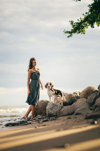 Woman standing by dog at beach against sky