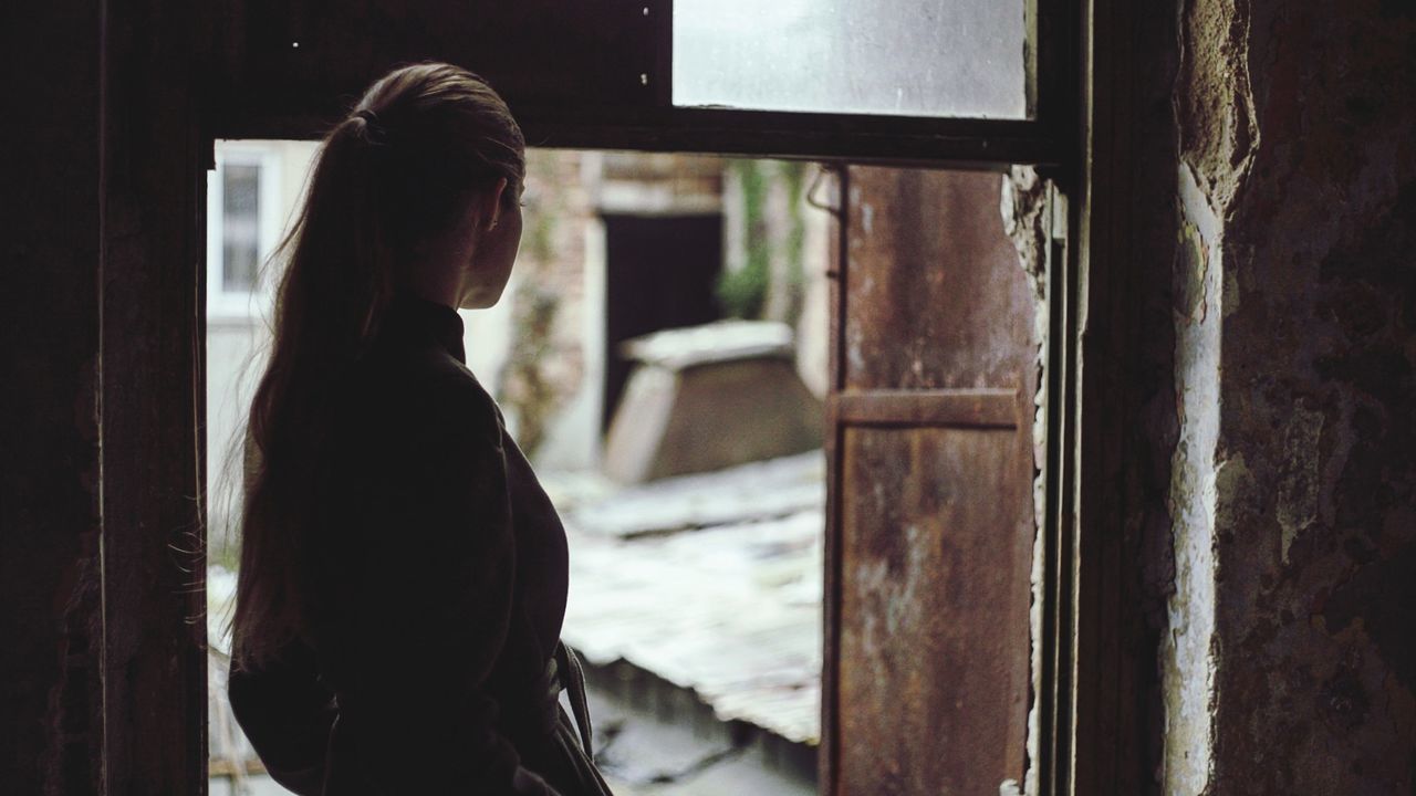 one person, standing, real people, window, indoors, women, lifestyles, waist up, adult, entrance, side view, architecture, door, looking, young adult, built structure, day, focus on foreground, leisure activity, hairstyle, contemplation