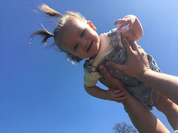 Cropped hands of father picking up cute daughter against clear blue sky