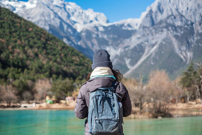 Rear view of woman standing by lake against mountains