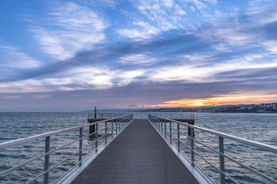 Footbridge over sea against sky during sunset