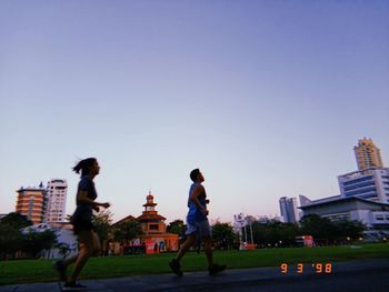 People by buildings against clear blue sky