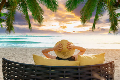 Rear view of woman relaxing on chair at beach