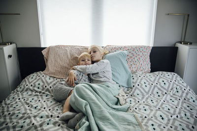 High angle portrait of sister embracing brother while lying on bed at home