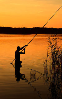 People fishing in lake at sunset