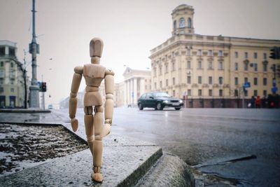 Wooden figurine on footpath in city against sky