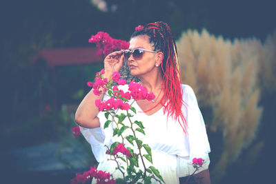 Young woman wearing sunglasses standing against pink flower