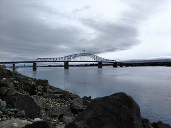 View of suspension bridge over river against cloudy sky