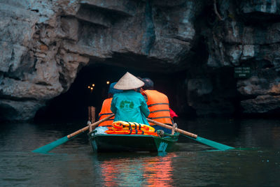 Rear view of person sitting on rock by river