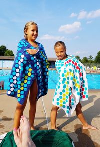 Happy siblings by swimming pool against sky